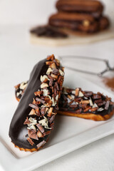 Plate with tasty chocolate eclairs on light table, closeup