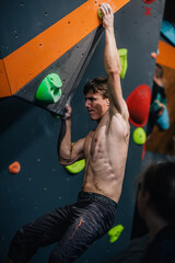 Fototapeta premium A young, athletic guy with a beautiful inflated body climbs a bouldering in a climbing hall. Emotions on the face.