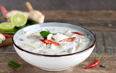 Thai spicy coconut soup Tom Kha with chicken, lemongrass, kaffir, chili, lime and on a wooden background.
