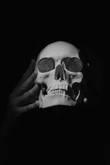 Skeleton skull with coins on the eyes as symbol of too busy human earning money and losEs living life. Vertical image.