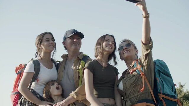 Caucasian family taking selfie on mobile phone while hiking. Happy parents and children making photo on mountain top. Mother in sunglasses holding smartphone. Modern technology, family, travel concept