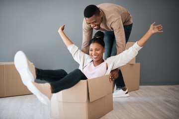 Couple, box and moving into real estate, home and fun while unpacking, playing and bond in a living room. House, fun and man with woman on a floor playful, laughing and celebrating their dream home
