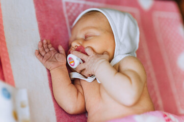 A beautiful newborn baby, a little girl lies, sleeps in bed, with a pacifier in her mouth, on a...