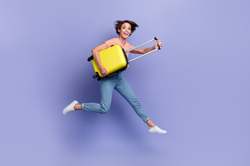 Fototapeta na wymiar Full length photo of sweet excited girl dressed orange t-shirt jumping high holding suitcase isolated purple color background