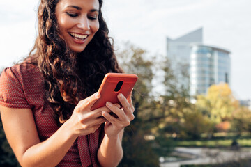 close up on hands of a smiling attractive latin american hispanic lady using phone in the city with...