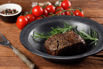 Medium rare roast beef with red tomatoes in a black plate on a rustic wooden table