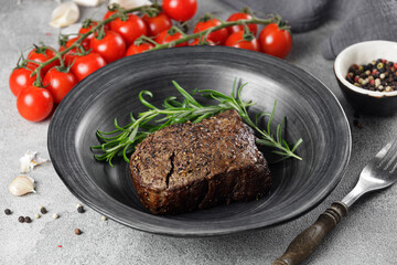 Medium rare roast beef with red tomatoes in a black plate on a marble table