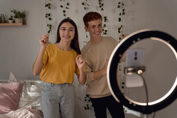 Teenage caucasian girl  and boy dancing and recording video using ring light