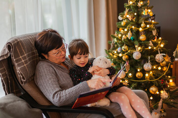 Granny and granddaughter reading a book near the Christmas tree