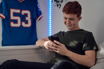 Caucasian teenage boy browsing phone while sitting on bed