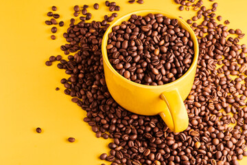 Cup of freshly brewed roasted coffee beans on yellow background