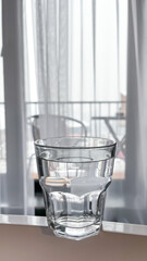 A small glass of water filled with water is placed on the table near the window.