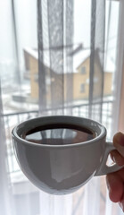 A woman drinks coffee in a house with windows. The girl enjoys the calm winter nature, travel, recreation.