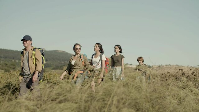 Happy family hiking on sunny day, exploring nature on vacation. Parents and children walking in row along trail path looking around, enjoying views. Tracking shot, slow motion. Family, travel concept.