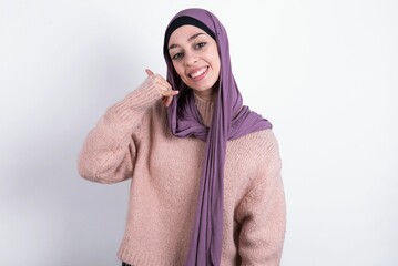 muslim woman wearing hijab and knitted sweater over white background smiling doing phone gesture with hand and fingers like talking on the telephone. Communicating concepts.