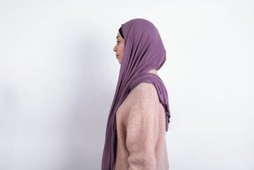 beautiful muslim woman wearing hijab and warm jumper over white background looking to side, relax...