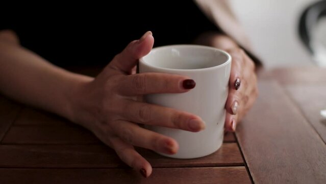 A cup of coffee and woman's hands with colored nails. Irritation, Excitement, Expecting. No face.
