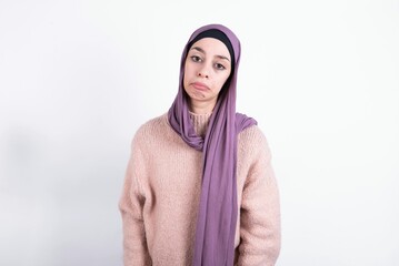 Displeased upset beautiful muslim woman wearing hijab and warm jumper over white wall frowns face as going to cry, being discontent and unhappy as can't achieve goals,  Disappointed model has troubles