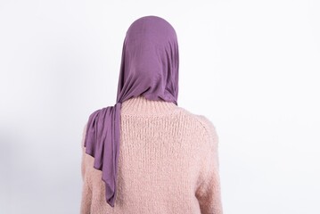 The back view of a beautiful muslim woman wearing hijab and warm jumper over white background ....