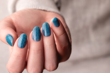 Female hand in gray knitted sweater with beautiful manicure - blue glitter nails. Nail care concept