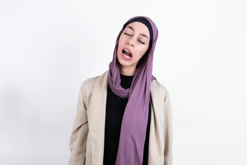 young beautiful muslim woman wearing hijab and jacket over white background yawns with opened mouth stands. Daily morning routine