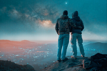 silhouette of two men embraced on top of the hill contemplating the night starry sky over the city