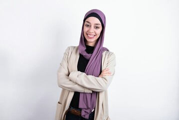 Portrait of charming young beautiful muslim woman wearing hijab and jacket over white background standing confidently smiling toothily with hands folded