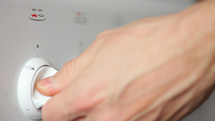 Hand of woman turning switch to side to turn on gas burner against blurred hob. Housewife prepares kitchen stove to cook dinner at home closeup