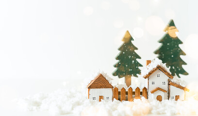 Fototapeta na wymiar Happy New Year and Merry Christmas postcard. Festive white background with toy wooden house, snow, light bokeh, christmas tree, village and decoration. Copy space for winter holidays greeting card. 