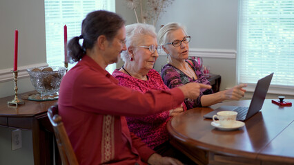 Elderly senior mother with mature son and daughter in law in dining room sitting in front of laptop computer looking at photos and talking about memories.