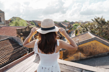 Fototapeta premium happy traveler traveling at Hoi An ancient town in Vietnam, woman with dress and hat sightseeing view at rooftop.landmark and popular for tourist attractions. Vietnam and Southeast Asia travel concept