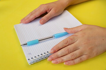 two female hands, white notepad, blue pen, yellow background