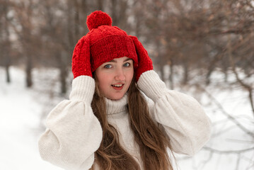 Happy blue-eyed girl in knitted red hat and mittens and woolen sweater in winter forest. Female knitwear