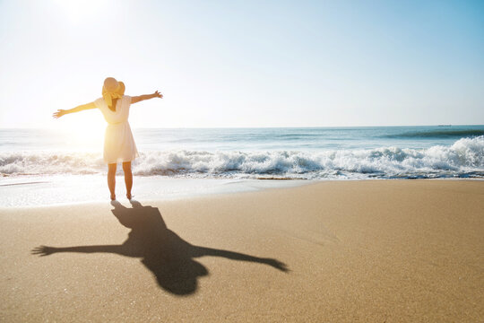 Happy woman standing on the beach with arms outstretched.