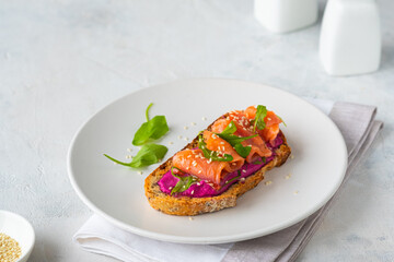 Open sandwich with beetroot puree, arugula and salted salmon on a white plate on a light concrete background. Recipes for sandwiches, smorrebrods.