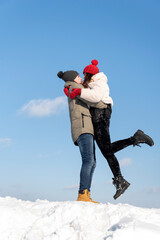 Fototapeta na wymiar Young couple is walking on winter day. Guy lifted his girlfriend. Portrait of couple in love against blue sky