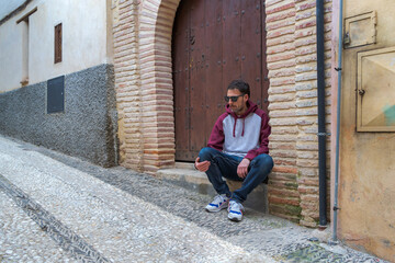 Young man sitting on the step of a house, outdoors, looking across the street.