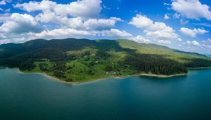 Fototapeta na wymiar Hotels on shores of lake with reflection of mountains Rhodope against cloudy sky. Panorama, top view
