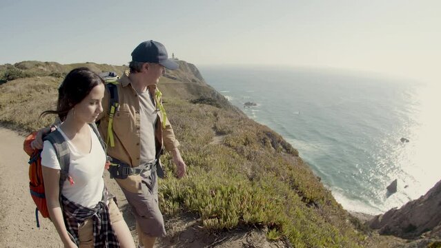 Father and daughter walking at mountain top, enjoying sea view. Caucasian family with backpacks hiking together, standing on cliff, spending vacation time. Slow motion. Travel, family concept.