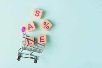 Shopping cart with wooden blocks with SALE letters blue background with copy space