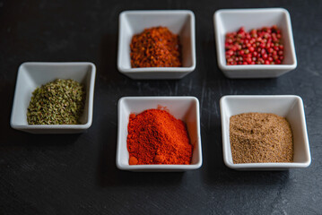 Spices in separate white bowls on a black background