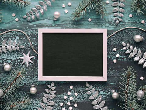 Xmas border with Christmas fir twigs, glass baubles and exotic fern leaves and light garland. Copy-space, text place on blackboard, chalk board. Flat lay, top view.