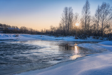 Sunset on a river with snow-covered icy banks. Ural, Russia.