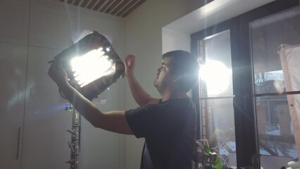 Side-view of brown-haired Caucasian male lighting technician adjusting stage lights on media production set indoors