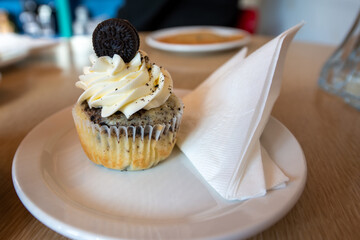 A chocolate cupcake with marshmallow chocolate icing and a store bought cookie sits on a wooden...