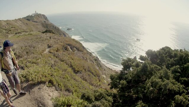 Father and daughter standing on cliff, enjoying view of sea. Family hiking at mountain top with backpacks on warm day, enjoying vacation together. Slow motion. Digital stab. Travel, family concept.