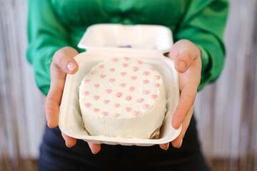 A girl in a green blouse holds a lunch box with a bento cake in her hands