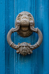 Closeup view of traditional vintage brass door knocker with face of man isolated on bright blue wooden door, Montpellier, France