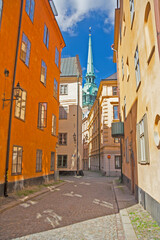 Fototapeta na wymiar Sweden - Stockholm - The view of charming narrow paved streets in old town Gamla Stan with german church (tyska kyrkan) spire in the distance