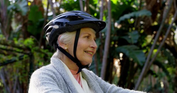Happy, senior woman and bike ride in a park with helmet, relax and smile while training, exercise and cardio cycle. Cycling, learning and active senior lady excited to practice riding in a forest